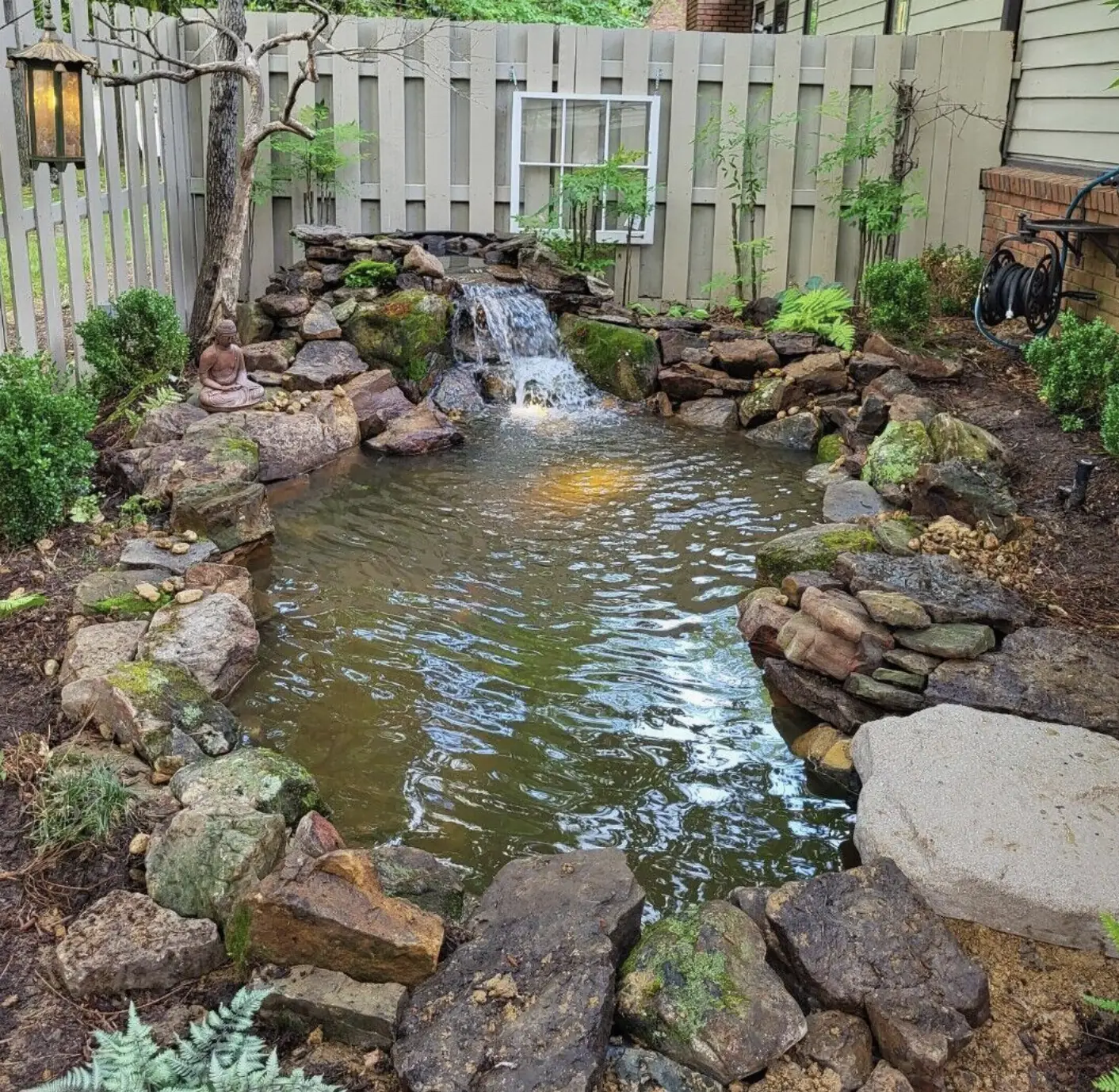 Backyard pond with a rock waterfall, small Buddha statue, and glowing underwater light