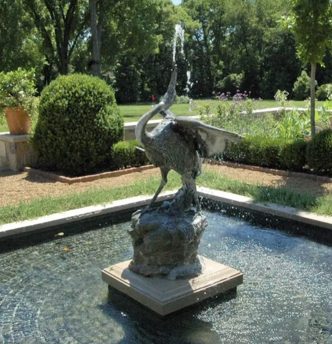 Bronze crane sculpture spraying water from its beak in a square tiled fountain basin