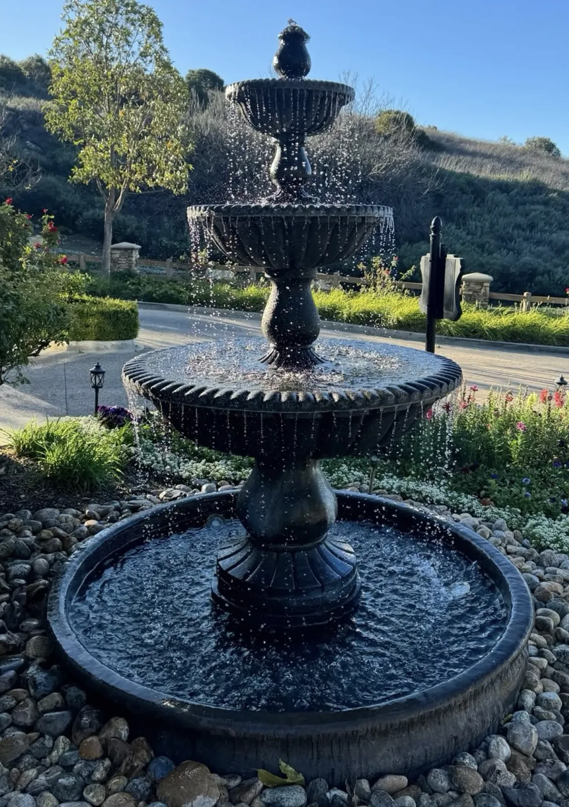 Dark bronze three-tier fountain running with curtains of water beside an entrance drive
