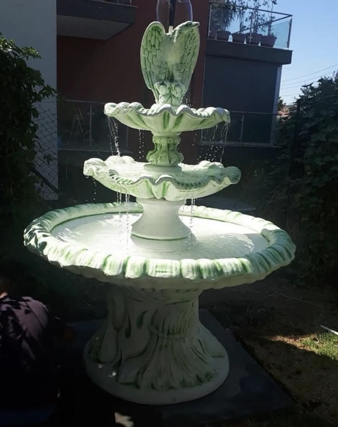 Three-tier white fountain streaked with green algae stains in a narrow side yard