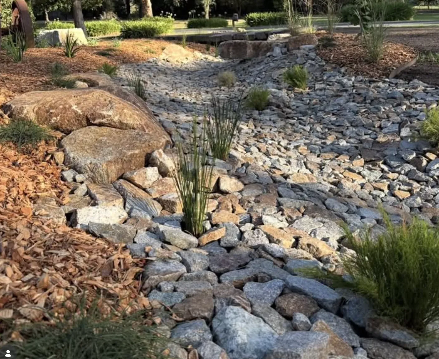Dry creek bed of angular granite riprap with young grasses at sunset