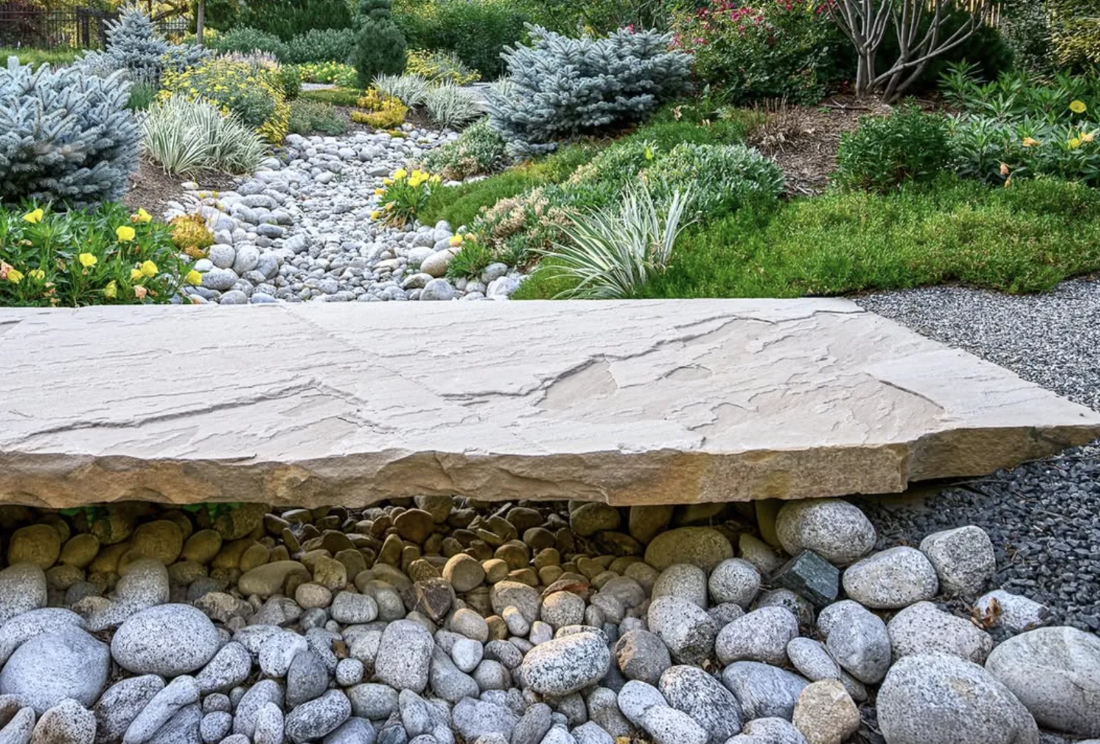 Flat flagstone slab bridging a dry creek bed of river rock in an ornamental garden
