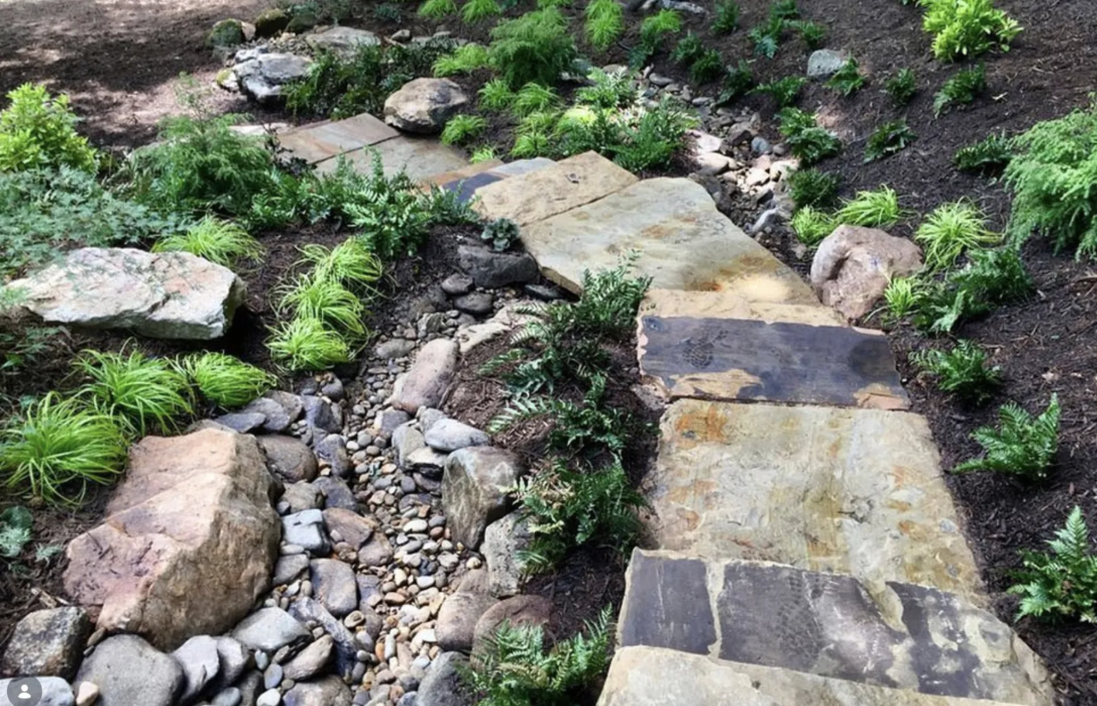 River rock dry creek bed carrying drainage past a raised deck with a flagstone crossing and path lights