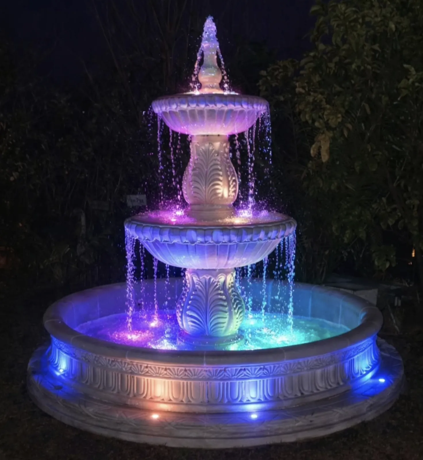 Three-tier fountain at night lit with color-changing LED lights in purple and blue