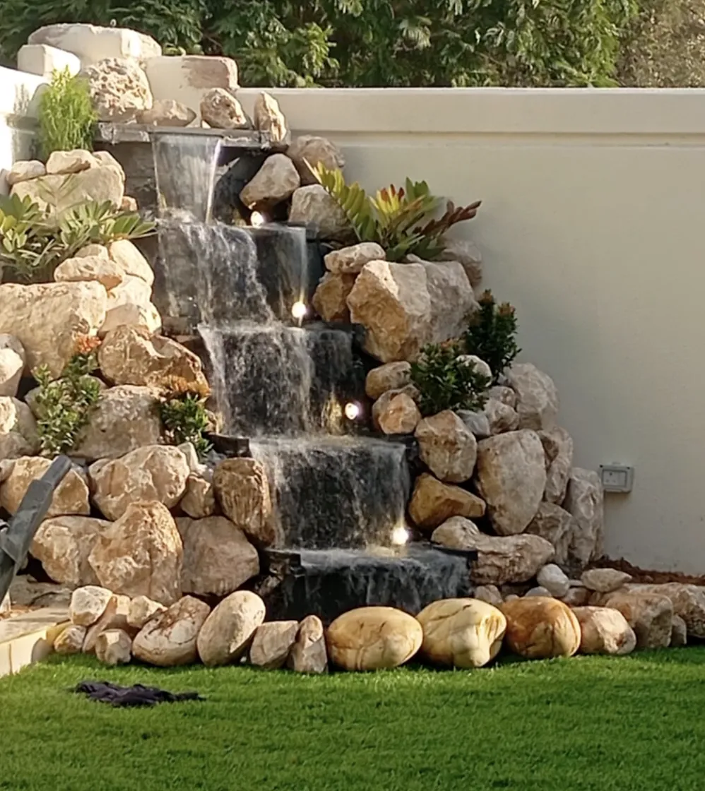 Five-tier rock waterfall with built-in lights cascading beside a white garden wall