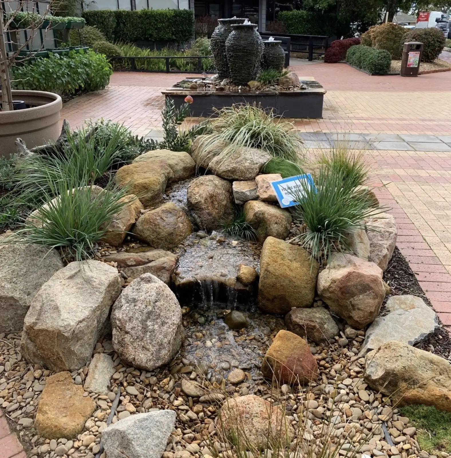 Small pondless waterfall with boulder surround and stacked stone urn fountains in the background
