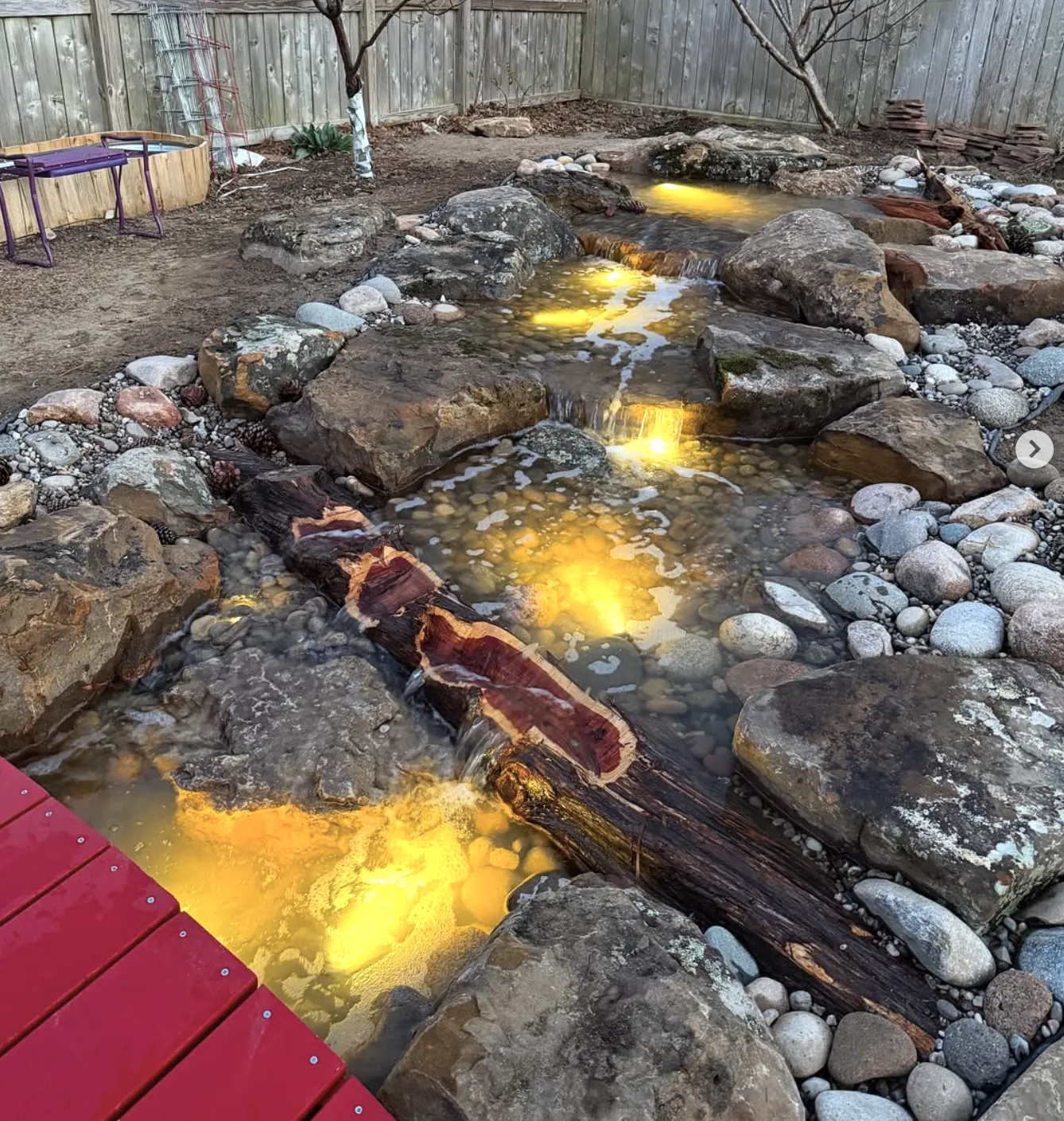 Shallow rock stream glowing with warm underwater lights, crossed by a split cedar log