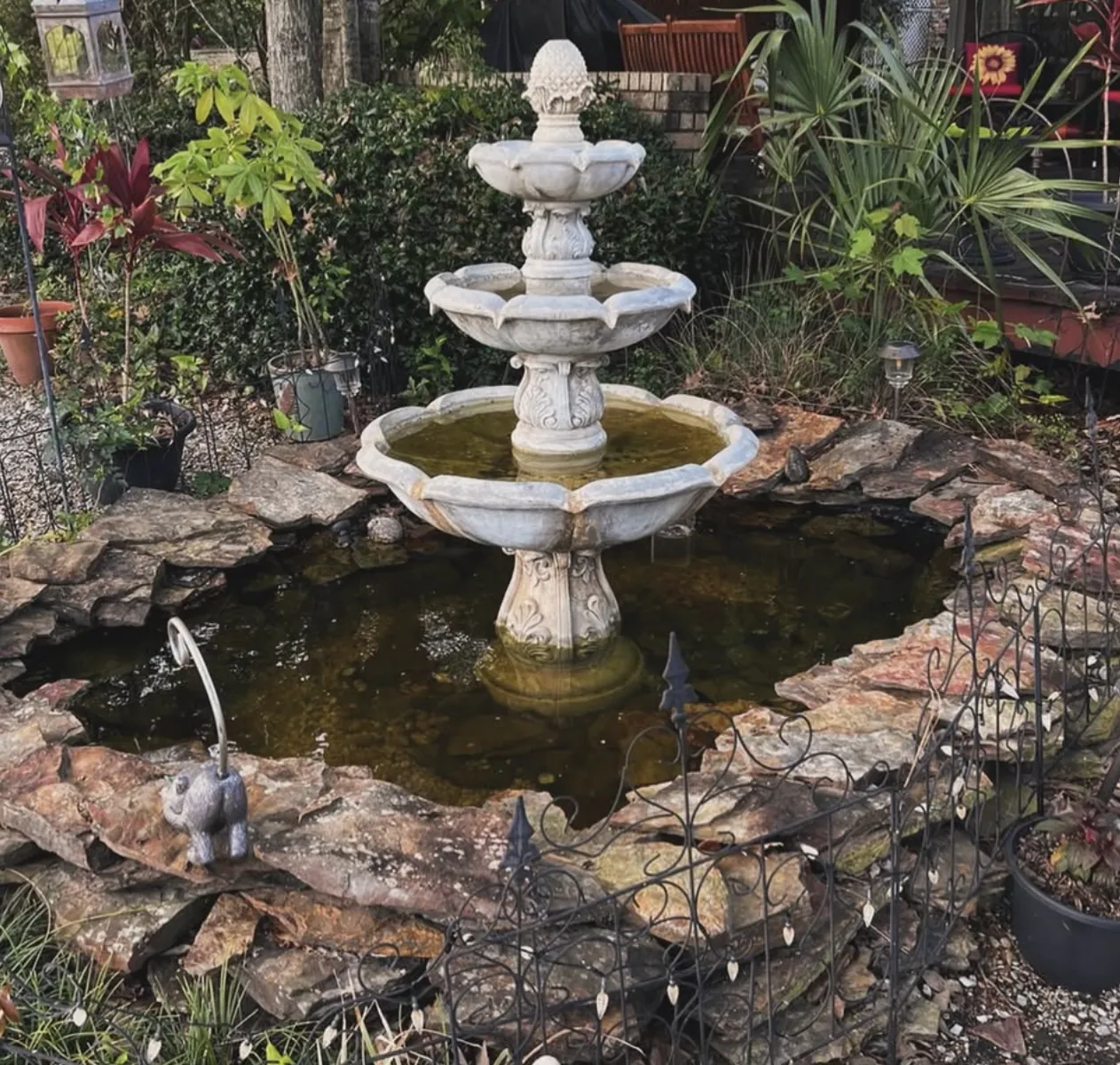 Three-tier concrete fountain with a pineapple finial standing in a rock-edged garden pond
