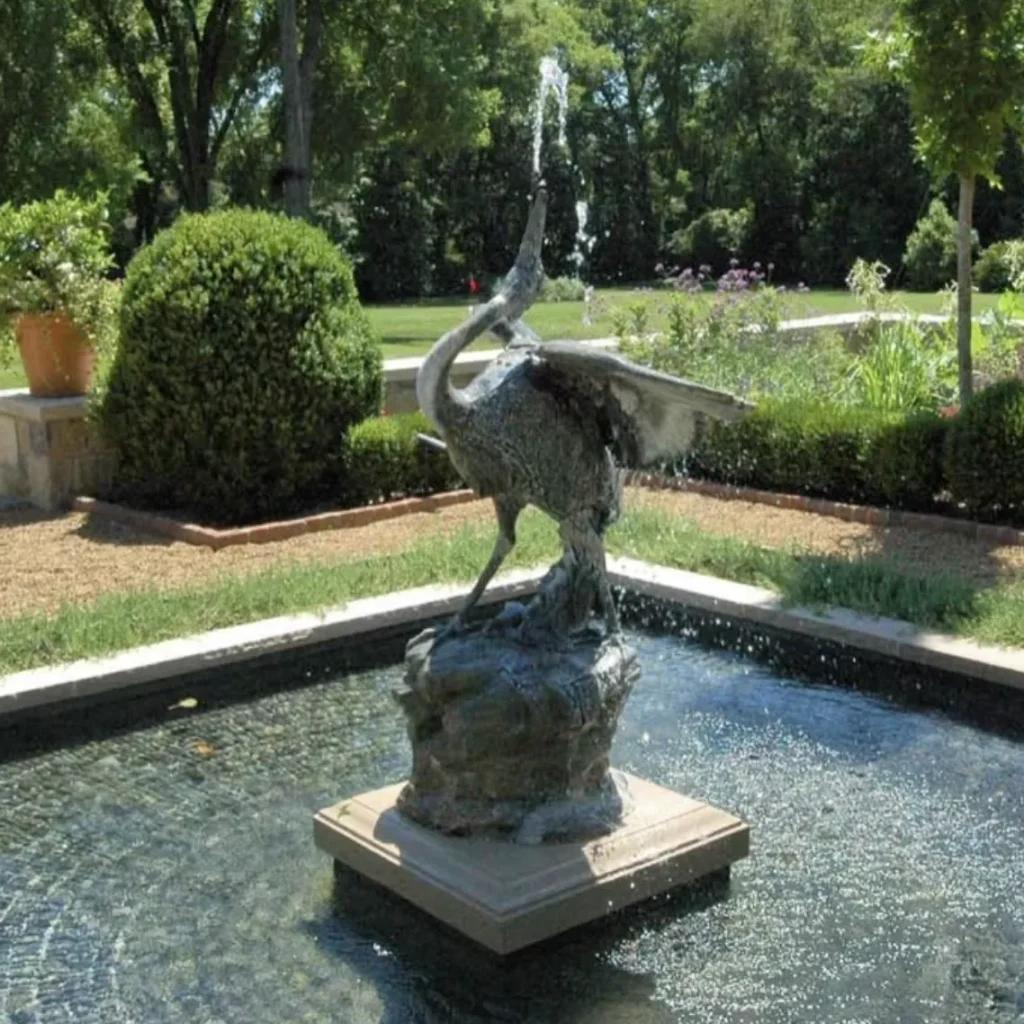 Bronze crane sculpture spraying water from its beak in a square tiled fountain basin