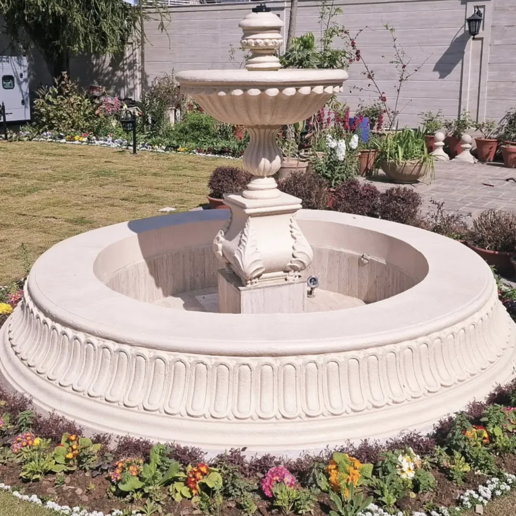 Large classical stone fountain standing in an empty carved basin on a lawn during installation