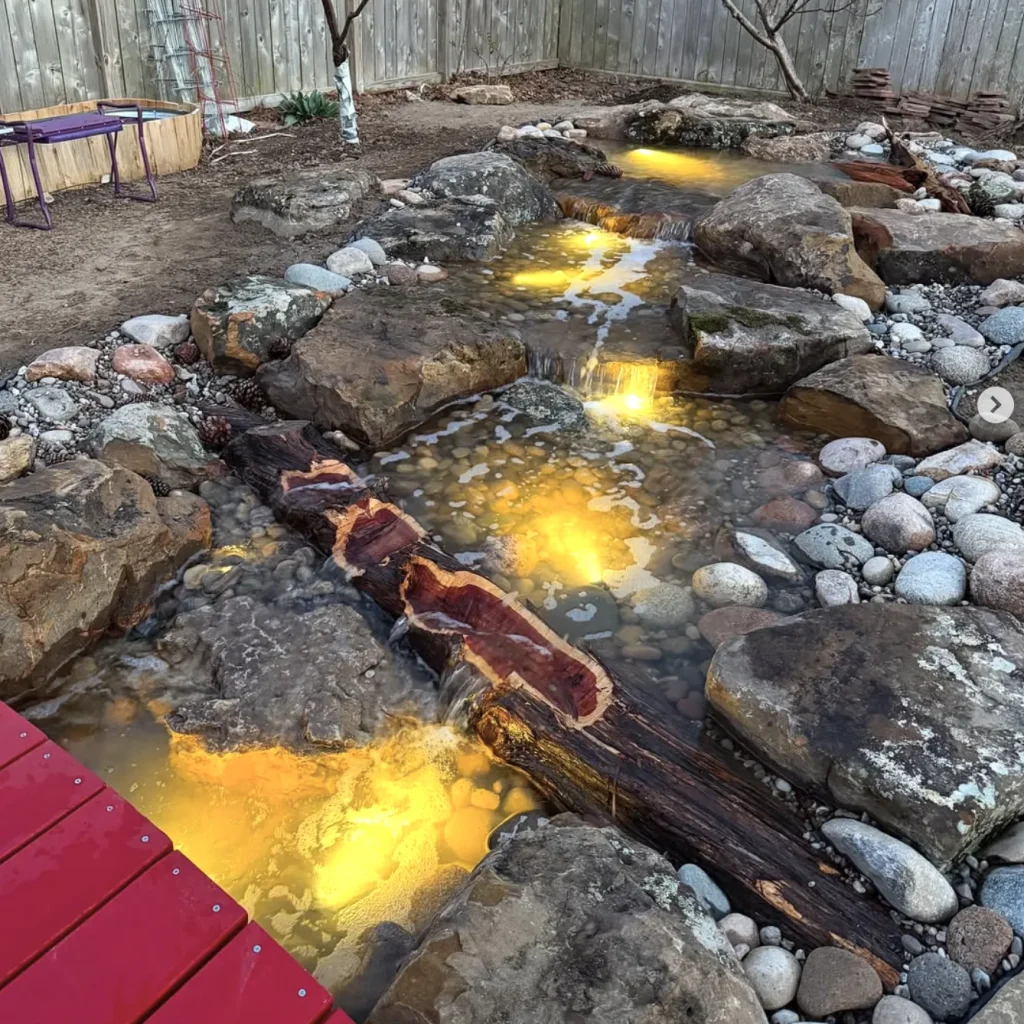 Shallow rock stream glowing with warm underwater lights, crossed by a split cedar log